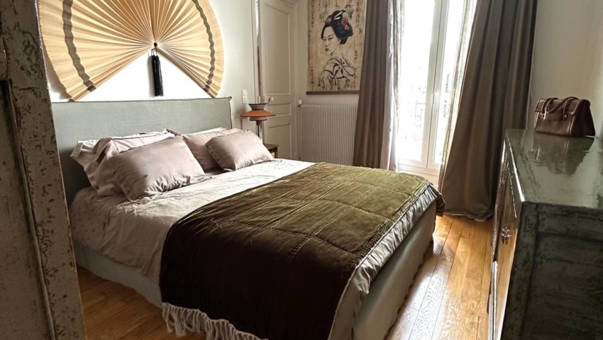 Chambre à coucher chaleureuse avec un lit marron, un parquet, une grande décoration murale représentant un ventilateur et la lumière du soleil qui pénètre par de grandes fenêtres. Canape Paris by Atelier Bis