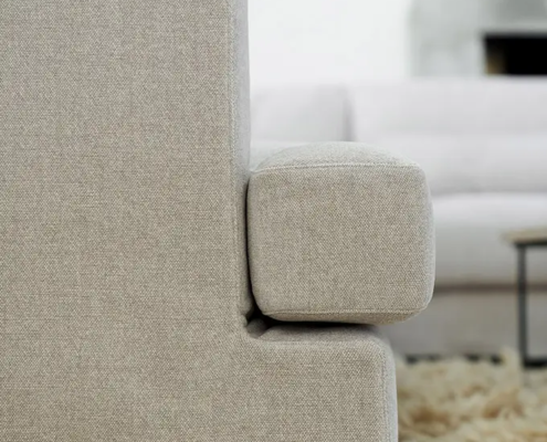 Vue latérale en gros plan d'un canapé beige rembourré sur un tapis beige à poils ras, avec un autre canapé à l'arrière-plan. Canape Paris by Atelier Bis