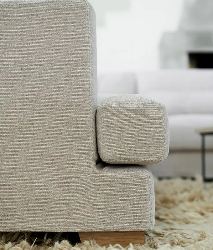 Vue latérale en gros plan d'un canapé beige rembourré sur un tapis beige à poils ras, avec un autre canapé à l'arrière-plan. Canape Paris by Atelier Bis