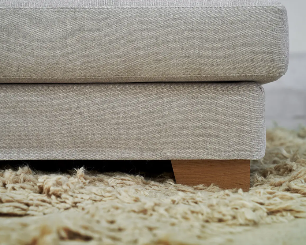 Gros plan sur un canapé en tissu beige avec des pieds en bois sur un tapis shag texturé marron clair. Canape Paris by Atelier Bis