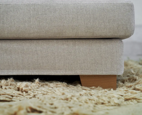 Gros plan sur un canapé en tissu beige avec des pieds en bois sur un tapis shag texturé marron clair. Canape Paris by Atelier Bis