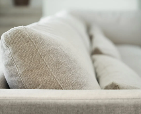 Vue rapprochée d'un canapé en tissu beige clair avec des coussins moelleux, photographié à l'intérieur. Canape Paris by Atelier Bis