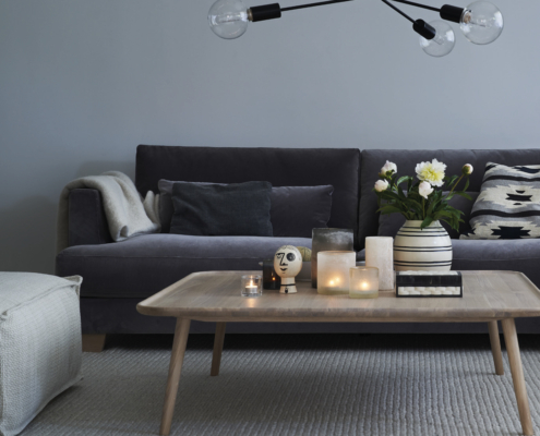 Salon moderne avec un canapé gris, une table basse en bois, des bougies, des fleurs et un plafonnier. Canape Paris by Atelier Bis