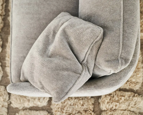 Gros plan sur un canapé gris avec un coussin assorti sur un tapis beige texturé. Canape Paris by Atelier Bis
