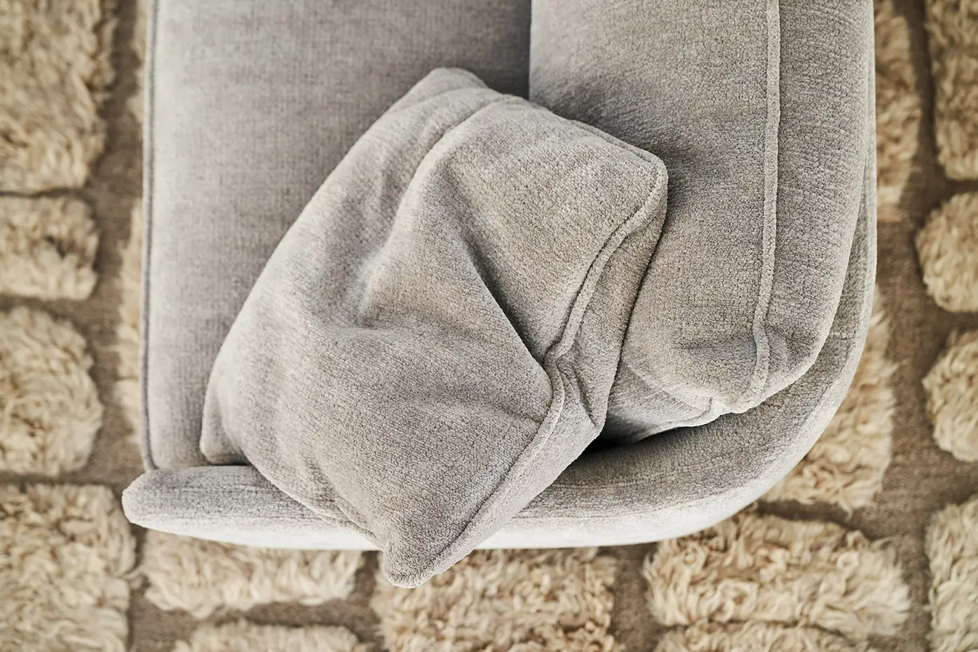 Gros plan sur un canapé gris avec un coussin assorti sur un tapis beige texturé. Canape Paris by Atelier Bis