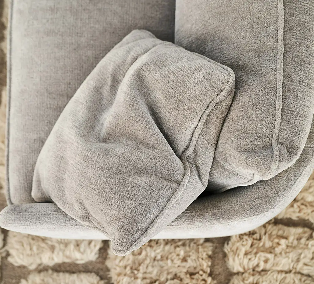 Un coussin gris repose sur un canapé gris, sous lequel se trouve un tapis beige texturé. Canape Paris by Atelier Bis