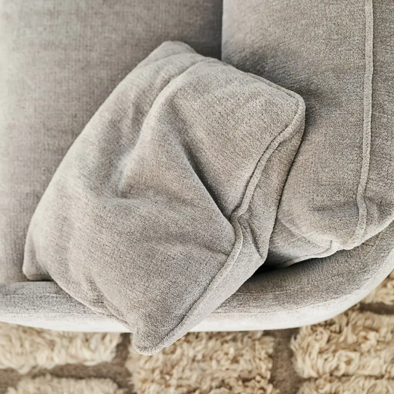 Un coussin gris repose sur un canapé gris, sous lequel se trouve un tapis beige texturé. Canape Paris by Atelier Bis