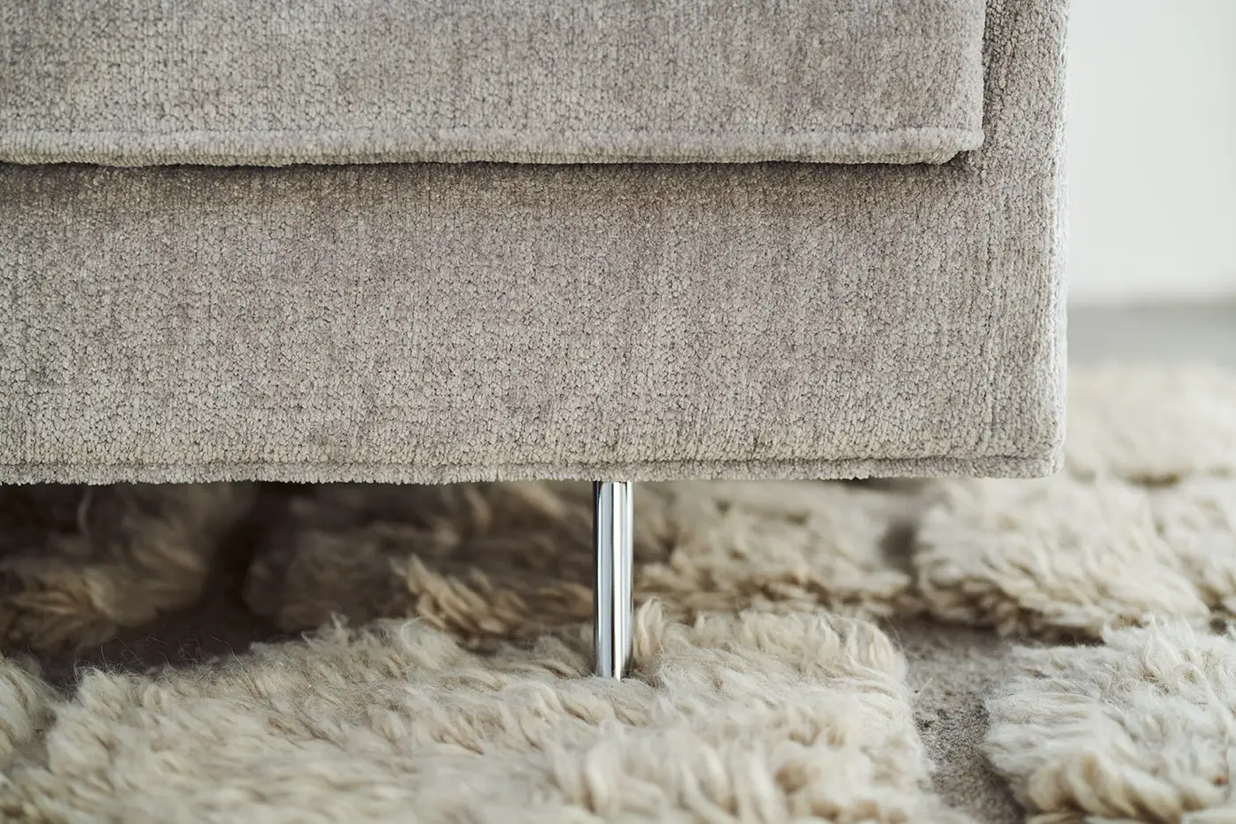 Gros plan sur un canapé beige avec un pied en métal, posé sur un tapis moelleux de couleur claire. Canape Paris by Atelier Bis