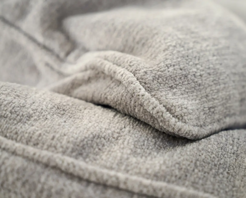Gros plan sur un tissu molletonné gris clair, dont la texture et les plis sont visibles. Canape Paris by Atelier Bis
