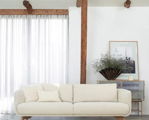 Salon minimaliste avec un canapé blanc, un tapis clair, des rideaux transparents et des œuvres d'art murales sur des murs blancs. Canape Paris by Atelier Bis