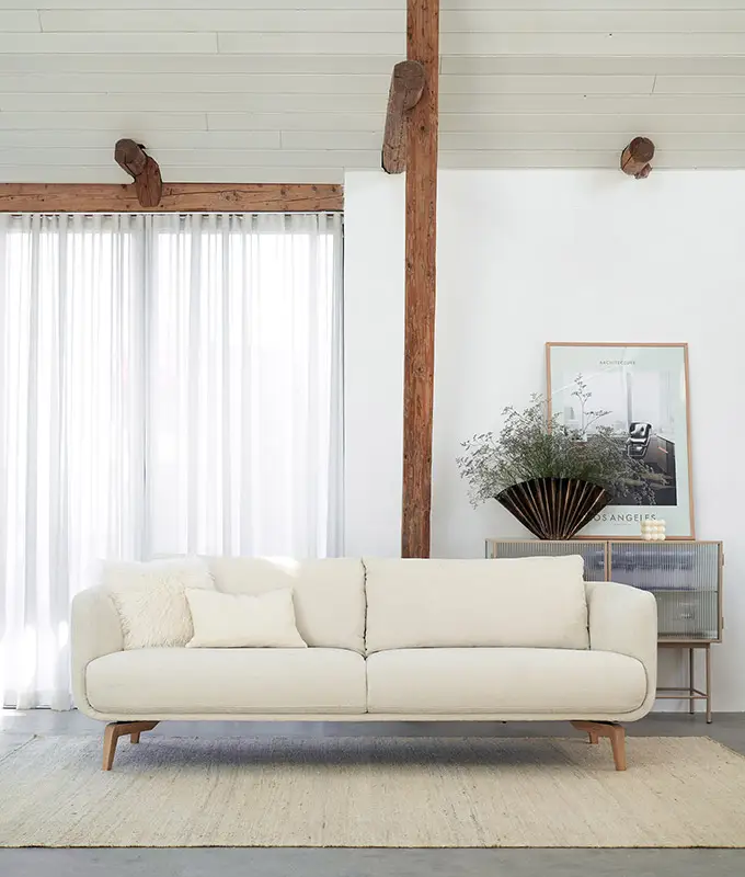 Salon minimaliste avec un canapé blanc, un tapis clair, des rideaux transparents et des œuvres d'art murales sur des murs blancs. Canape Paris by Atelier Bis