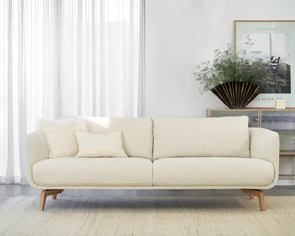 Canapé crème avec coussins dans un salon moderne et lumineux avec des rideaux transparents et une décoration minimaliste. Canape Paris by Atelier Bis