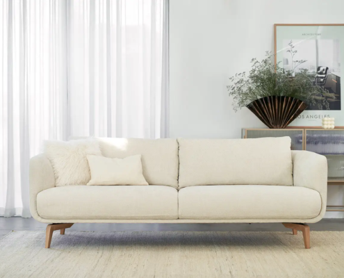 Canapé crème avec coussins dans un salon moderne et lumineux avec des rideaux transparents et une décoration minimaliste. Canape Paris by Atelier Bis