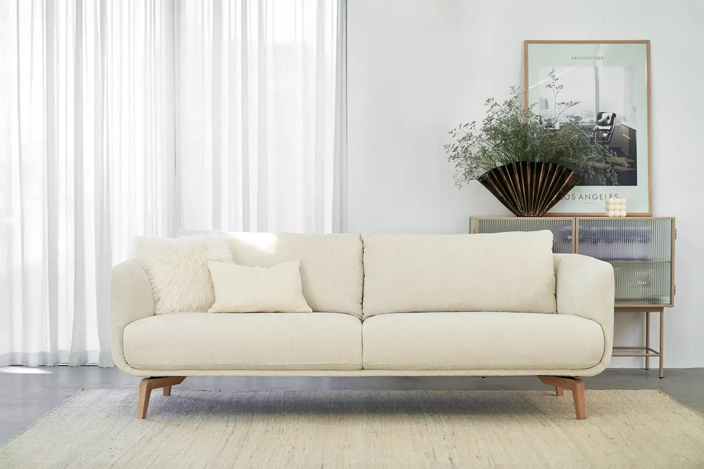 Canapé crème avec coussins dans un salon moderne et lumineux avec des rideaux transparents et une décoration minimaliste. Canape Paris by Atelier Bis