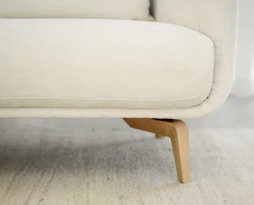 Gros plan sur un canapé beige rembourré avec des pieds en bois sur un tapis de couleur claire. Canape Paris by Atelier Bis