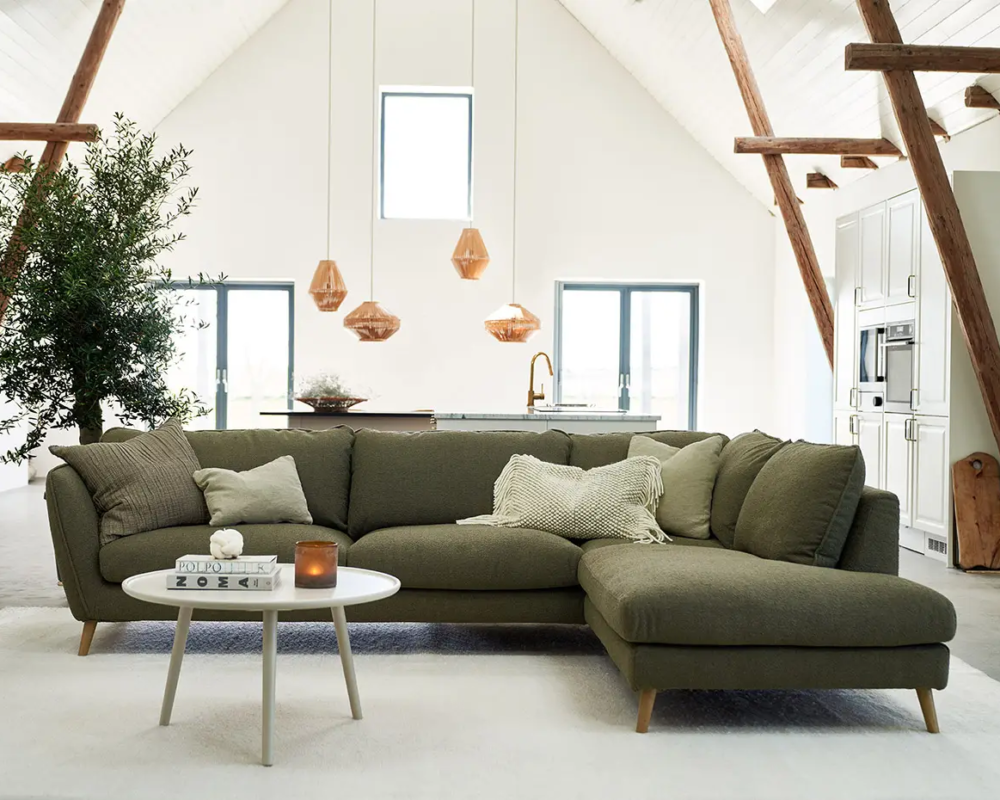 Salon loft moderne avec canapé sectionnel vert, table basse ronde, plantes et lampes suspendues. Canape Paris by Atelier Bis