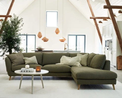 Salon loft moderne avec canapé sectionnel vert, table basse ronde, plantes et lampes suspendues. Canape Paris by Atelier Bis