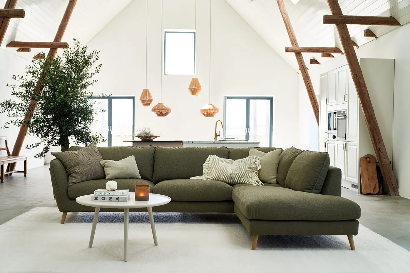 Salon moderne avec un canapé sectionnel vert, une table basse, des lampes suspendues et un plafond voûté. Canape Paris by Atelier Bis