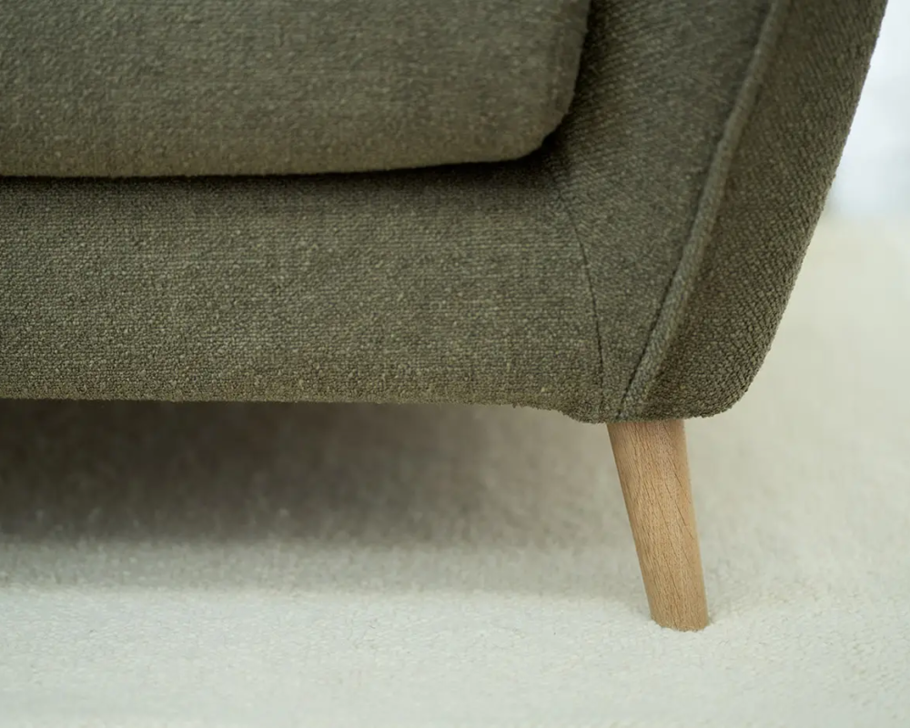 Gros plan sur un canapé en tissu vert avec des pieds en bois sur une moquette blanche. Canape Paris by Atelier Bis