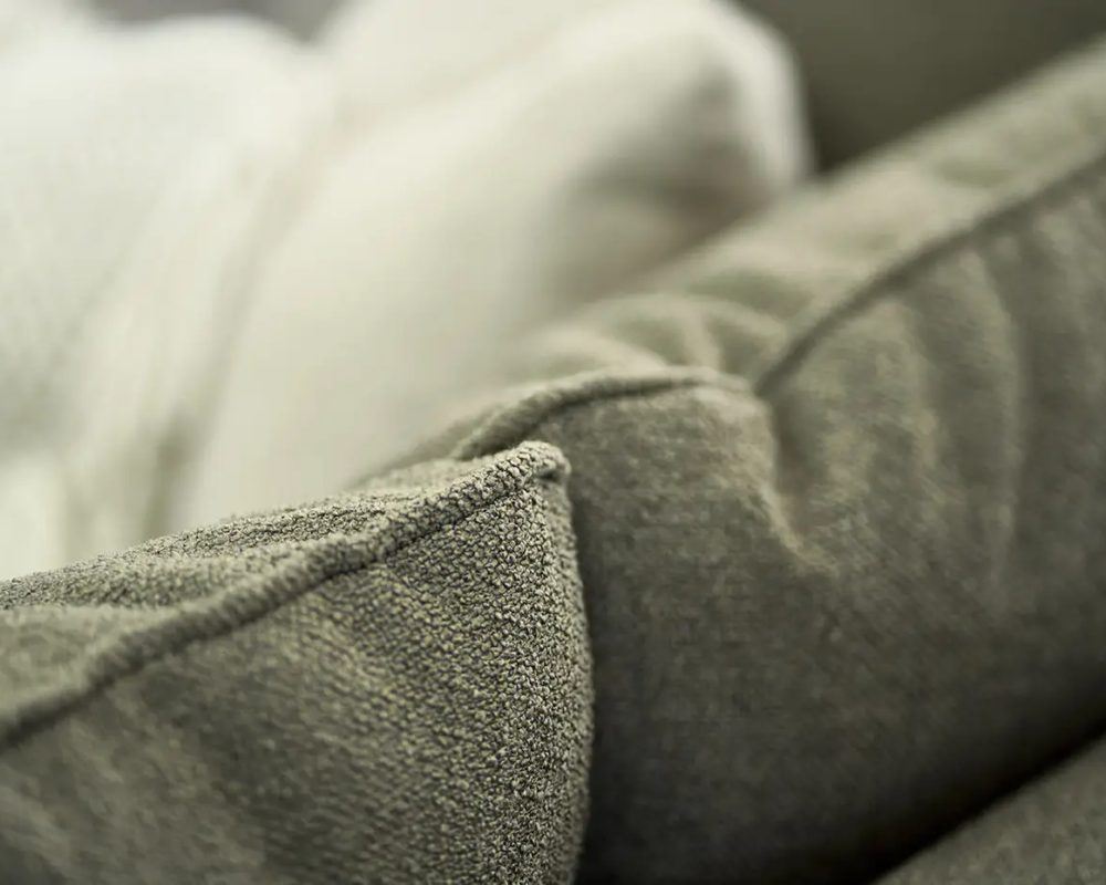 Gros plan d'un coussin de canapé gris texturé avec une couverture de couleur crème en arrière-plan. Canape Paris by Atelier Bis