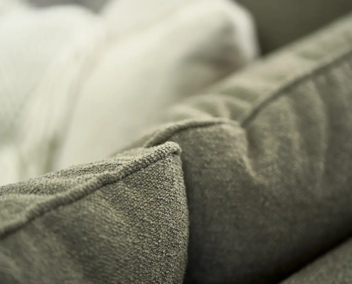 Gros plan d'un coussin de canapé gris texturé avec une couverture de couleur crème en arrière-plan. Canape Paris by Atelier Bis