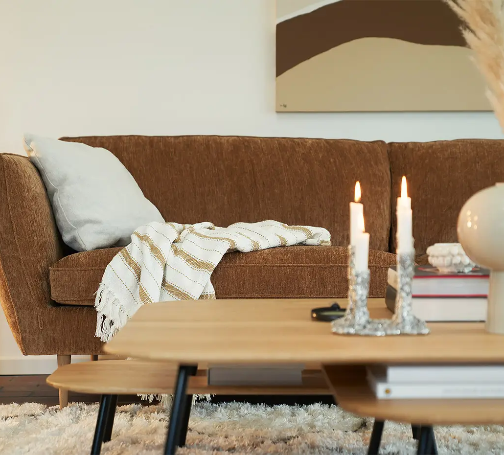 Canapé marron avec une couverture rayée, table basse avec des bougies et un cactus en pot dans un salon confortable. Canape Paris by Atelier Bis