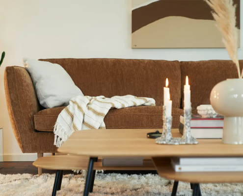 Canapé marron avec une couverture rayée, table basse avec des bougies et un cactus en pot dans un salon confortable. Canape Paris by Atelier Bis