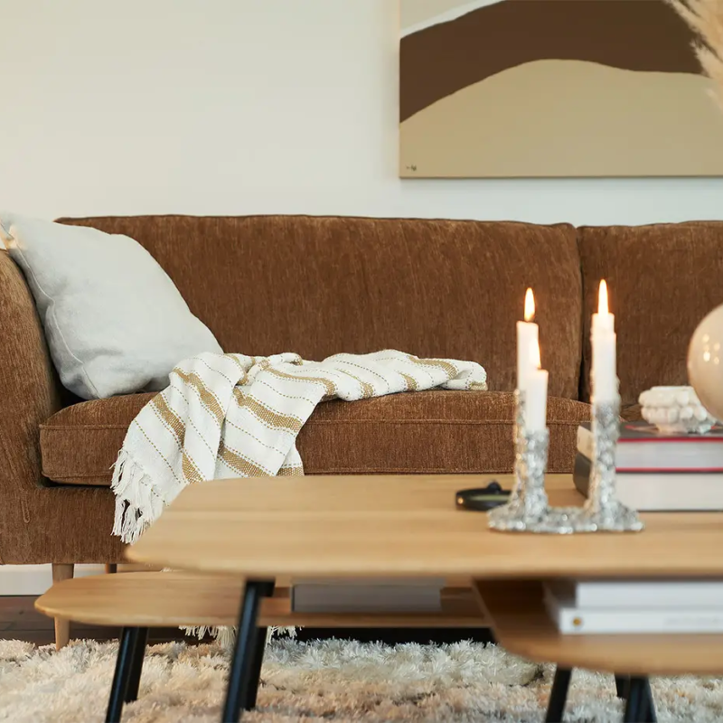 Canapé marron avec une couverture rayée, table basse avec des bougies et un cactus en pot dans un salon confortable. Canape Paris by Atelier Bis