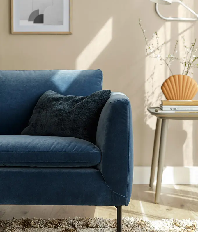 Salon moderne avec un canapé bleu, un coussin noir, une table d'appoint et des œuvres d'art murales sous la lumière naturelle du soleil. Canape Paris by Atelier Bis