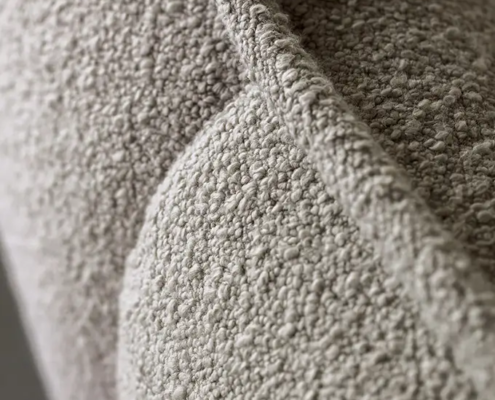 Gros plan d'un tissu bouclé texturé, gris clair, sur une surface matelassée avec des détails de couture visibles. Canape Paris by Atelier Bis