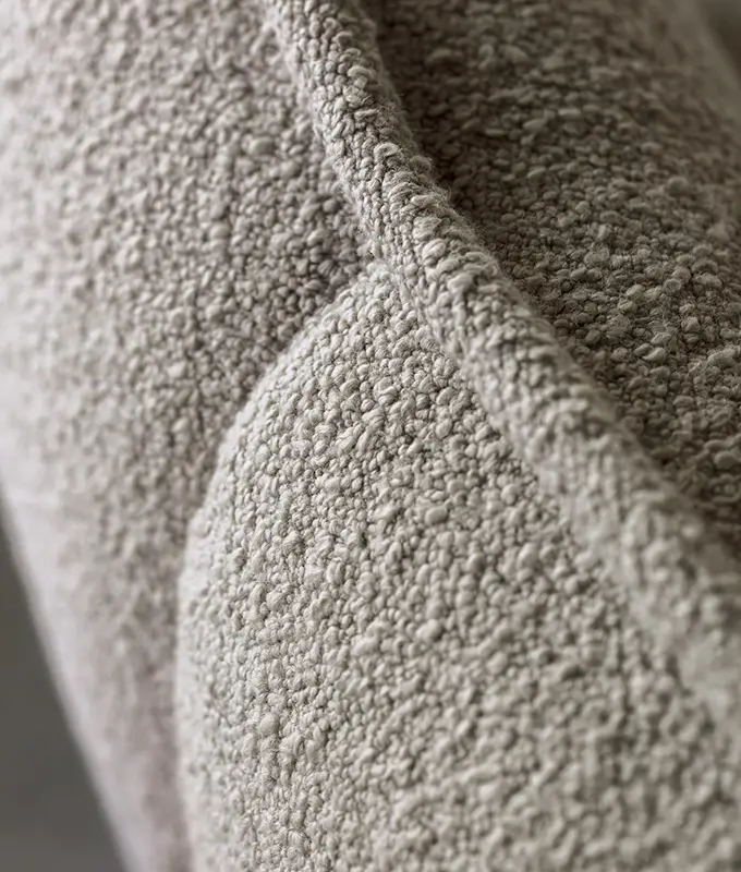 Gros plan d'un tissu bouclé texturé, gris clair, sur une surface matelassée avec des détails de couture visibles. Canape Paris by Atelier Bis