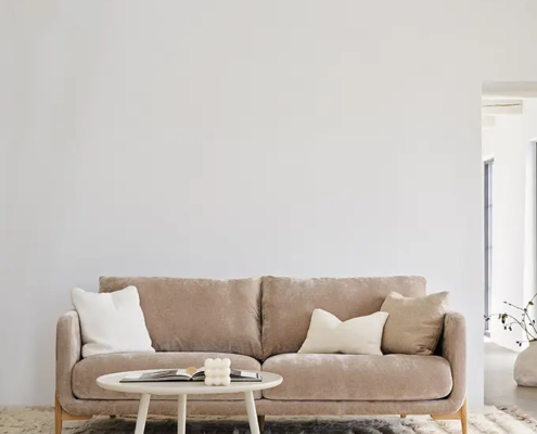 Canapé beige avec des coussins blancs, une table basse ronde et un tapis texturé dans un salon minimaliste. Canape Paris by Atelier Bis