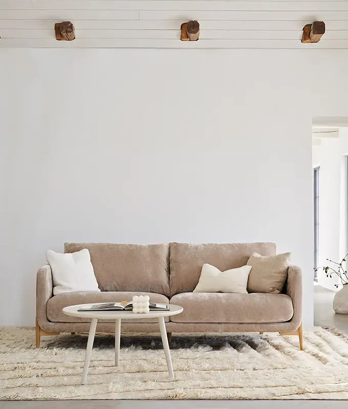 Canapé beige avec des coussins blancs, une table basse ronde et un tapis texturé dans un salon minimaliste. Canape Paris by Atelier Bis