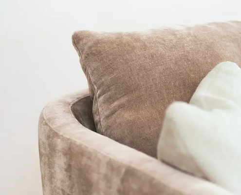 Gros plan sur un canapé en velours beige avec deux coussins, l'un beige et l'autre blanc cassé, sur un fond clair. Canape Paris by Atelier Bis