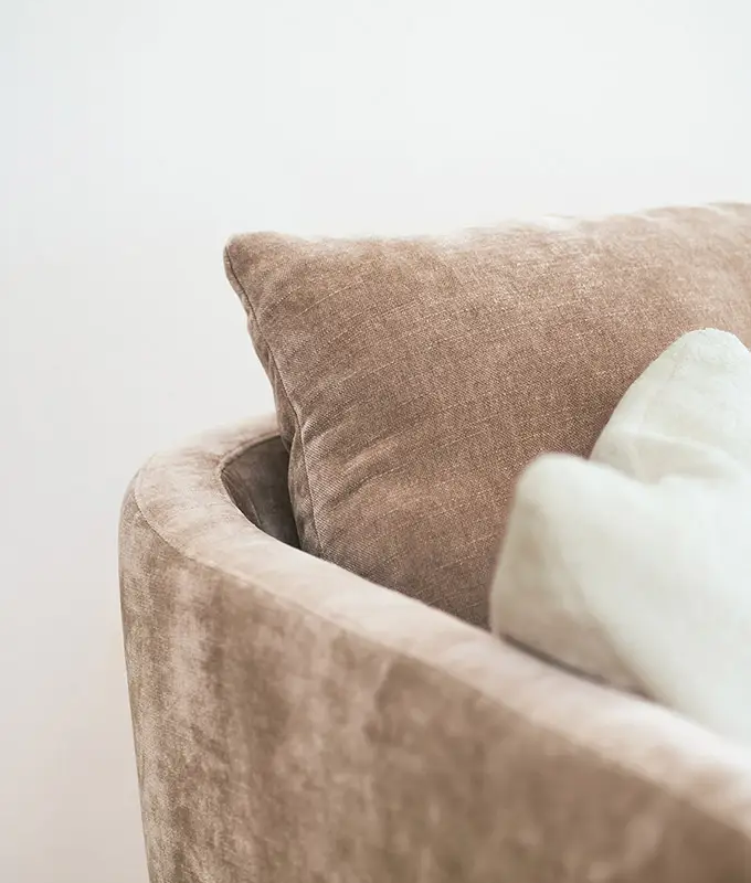 Gros plan sur un canapé en velours beige avec deux coussins, l'un beige et l'autre blanc cassé, sur un fond clair. Canape Paris by Atelier Bis