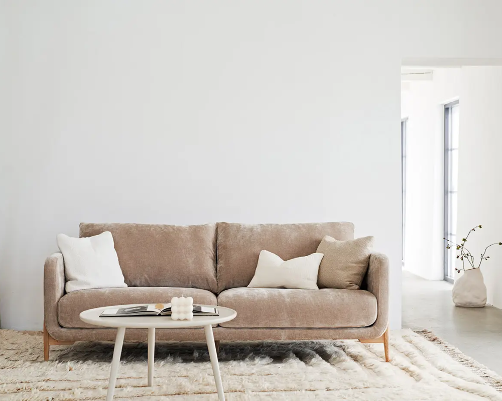 Canapé beige avec coussins blancs et table ronde dans un salon lumineux et minimaliste. Canape Paris by Atelier Bis