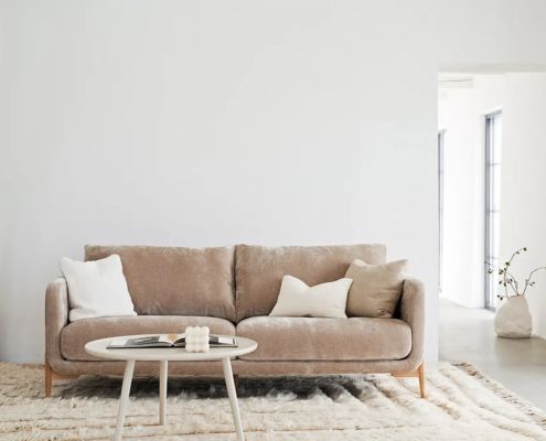 Canapé beige avec coussins blancs et table ronde dans un salon lumineux et minimaliste. Canape Paris by Atelier Bis