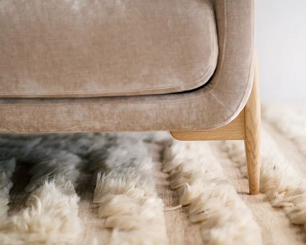 Gros plan sur un pied de canapé beige posé sur un tapis moelleux de couleur crème. Canape Paris by Atelier Bis