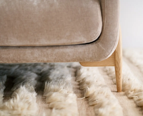 Gros plan sur un pied de canapé beige posé sur un tapis moelleux de couleur crème. Canape Paris by Atelier Bis