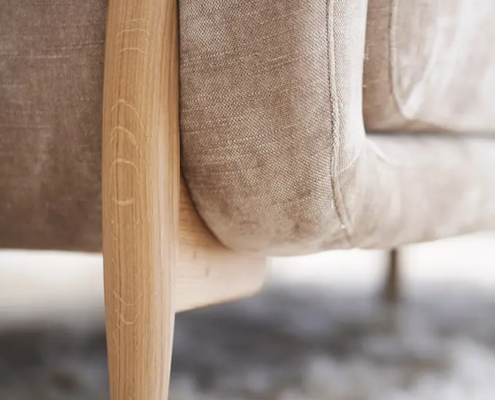 Gros plan sur un canapé en tissu beige avec des pieds en bois, posé sur un tapis blanc doux et moelleux. Canape Paris by Atelier Bis