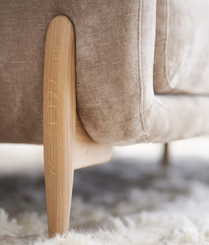 Gros plan sur un canapé en tissu beige avec des pieds en bois, posé sur un tapis blanc doux et moelleux. Canape Paris by Atelier Bis