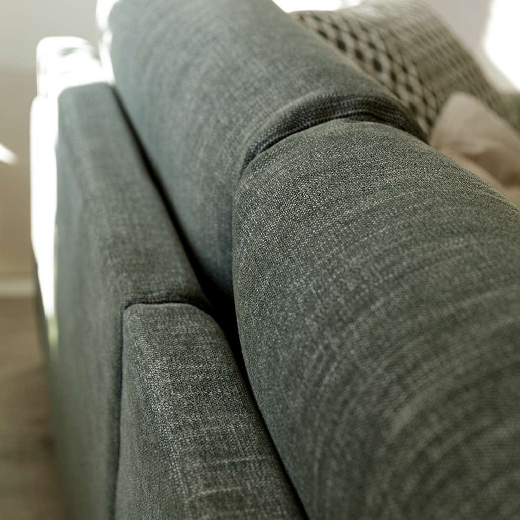 Gros plan sur un canapé en tissu gris avec des coussins à la lumière du soleil. Canape Paris by Atelier Bis