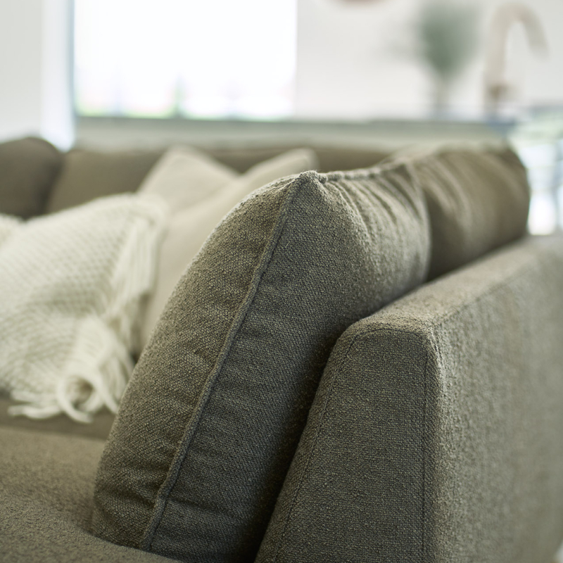 Gros plan sur un canapé en tissu gris avec un plaid blanc dans un salon lumineux. Canape Paris by Atelier Bis