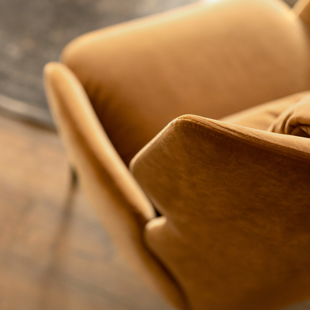 Gros plan d'un fauteuil moderne du milieu du siècle, de couleur beige, posé sur un sol en bois à côté d'un tapis foncé. Canape Paris by Atelier Bis