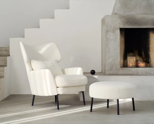 Fauteuil et ottoman blancs modernes à côté d'une cheminée en béton et d'un escalier minimaliste dans une pièce lumineuse. Canape Paris by Atelier Bis