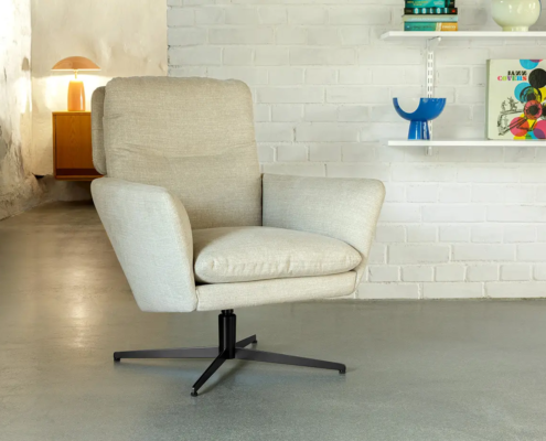 Fauteuil pivotant rembourré beige sur base métallique dans une pièce moderne avec des étagères et une lampe. Canape Paris by Atelier Bis
