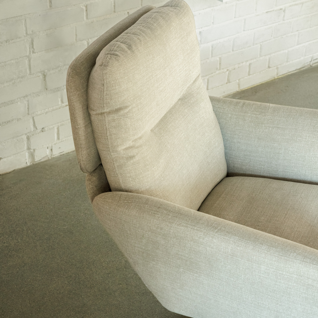 Fauteuil rembourré gris clair à haut dossier sur un sol gris clair près d'un mur de briques blanches. Canape Paris by Atelier Bis