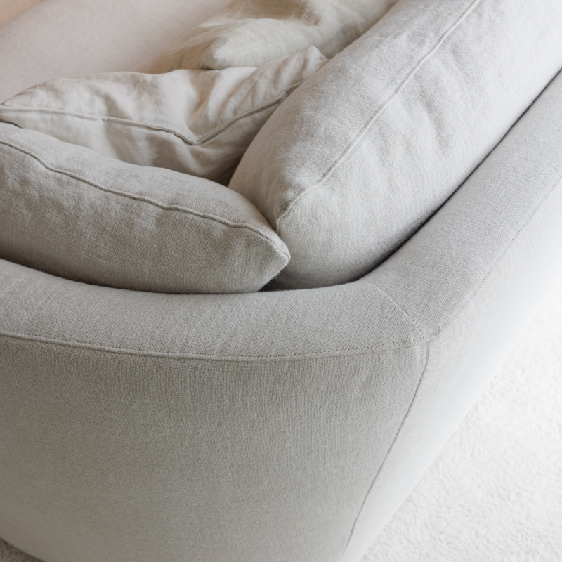 Gros plan sur un canapé moderne en tissu beige clair avec des coussins moelleux, posé sur un sol recouvert d'une moquette claire. Canape Paris by Atelier Bis