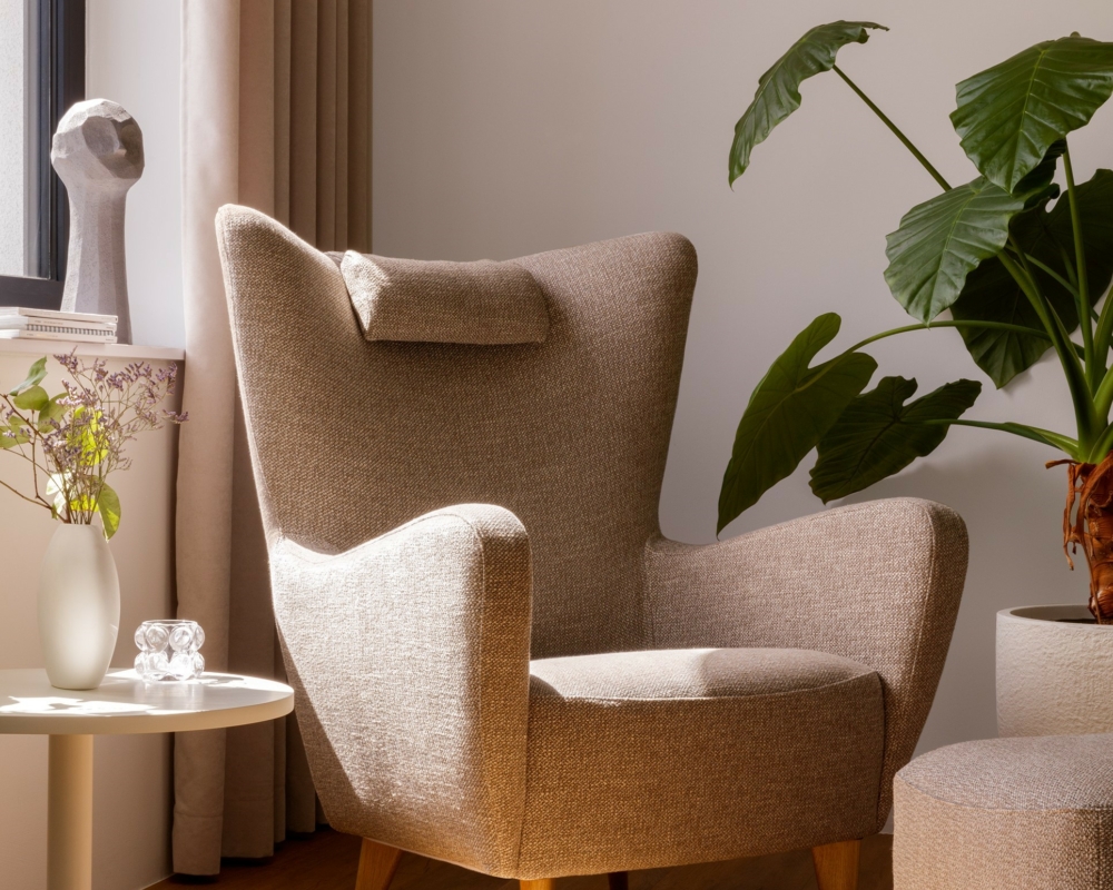 Fauteuil beige dans un coin ensoleillé avec une plante, une table d'appoint et un décor moderne sur un sol en bois. Canape Paris by Atelier Bis