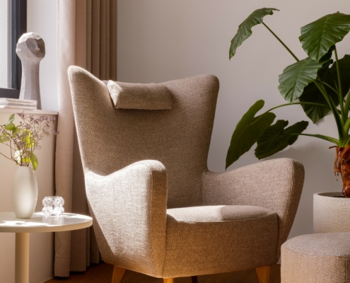 Fauteuil beige dans un coin ensoleillé avec une plante, une table d'appoint et un décor moderne sur un sol en bois. Canape Paris by Atelier Bis